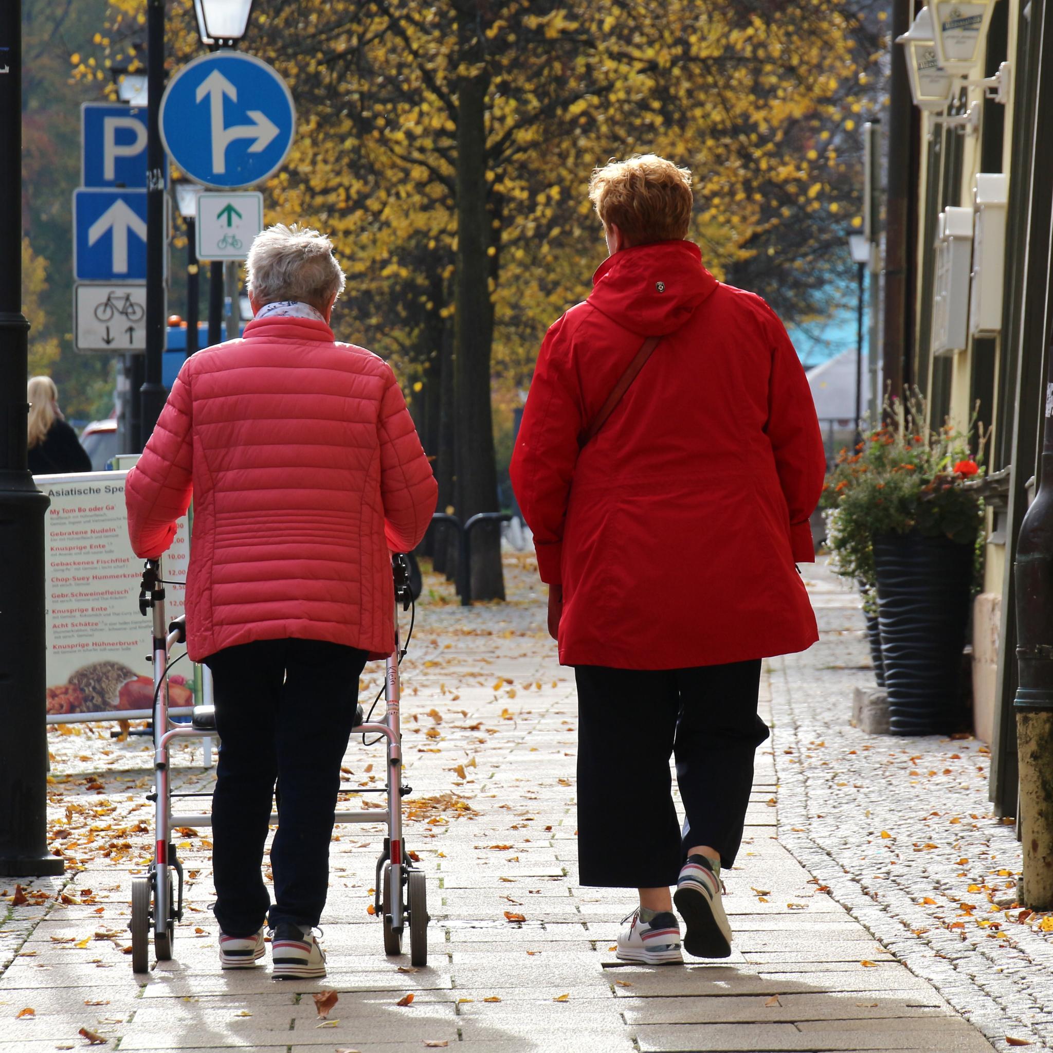 Ältere Frau mit Rollator und ihre Begleitperson gehen spazieren