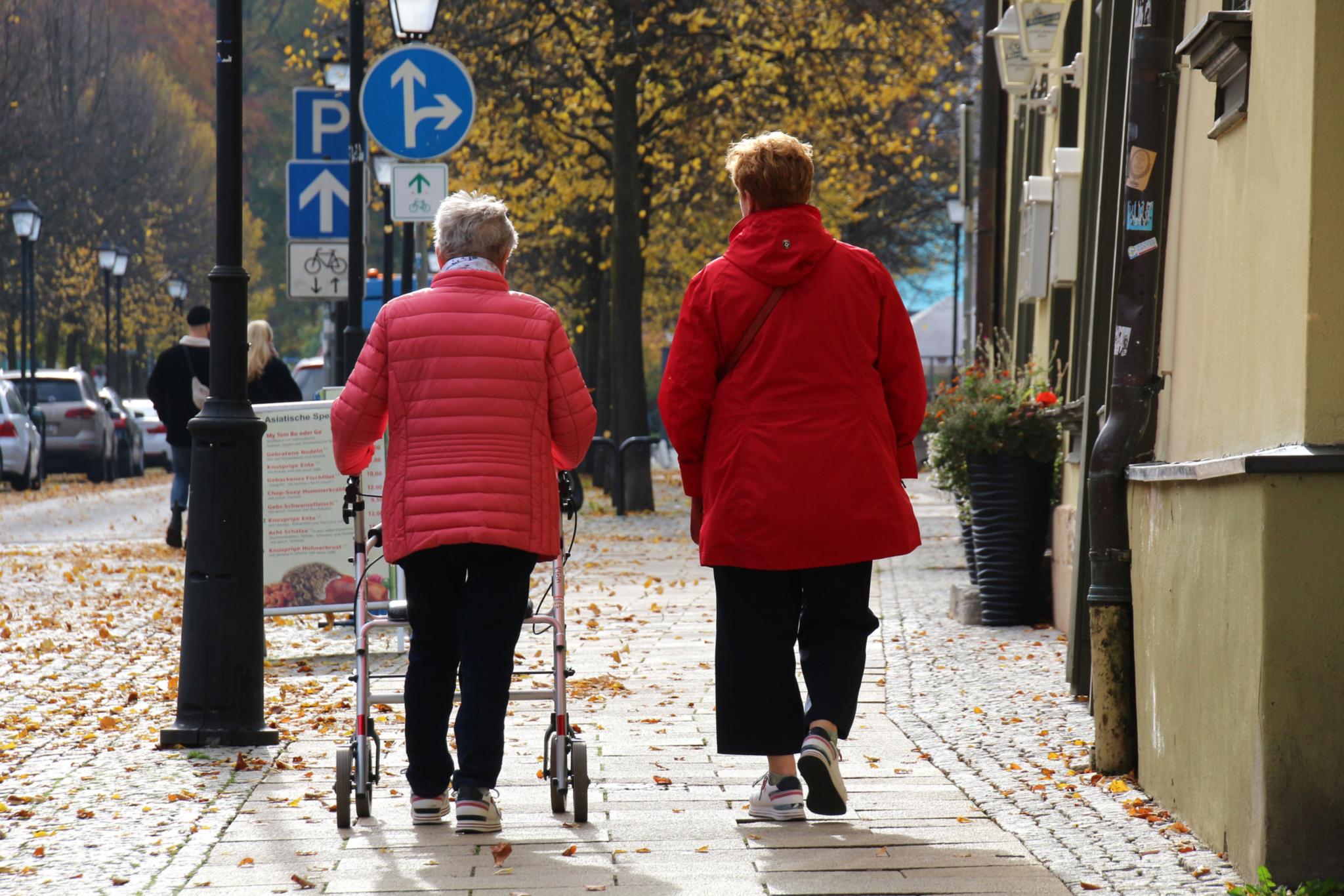 Ältere Frau mit Rollator und ihre Begleitperson gehen spazieren