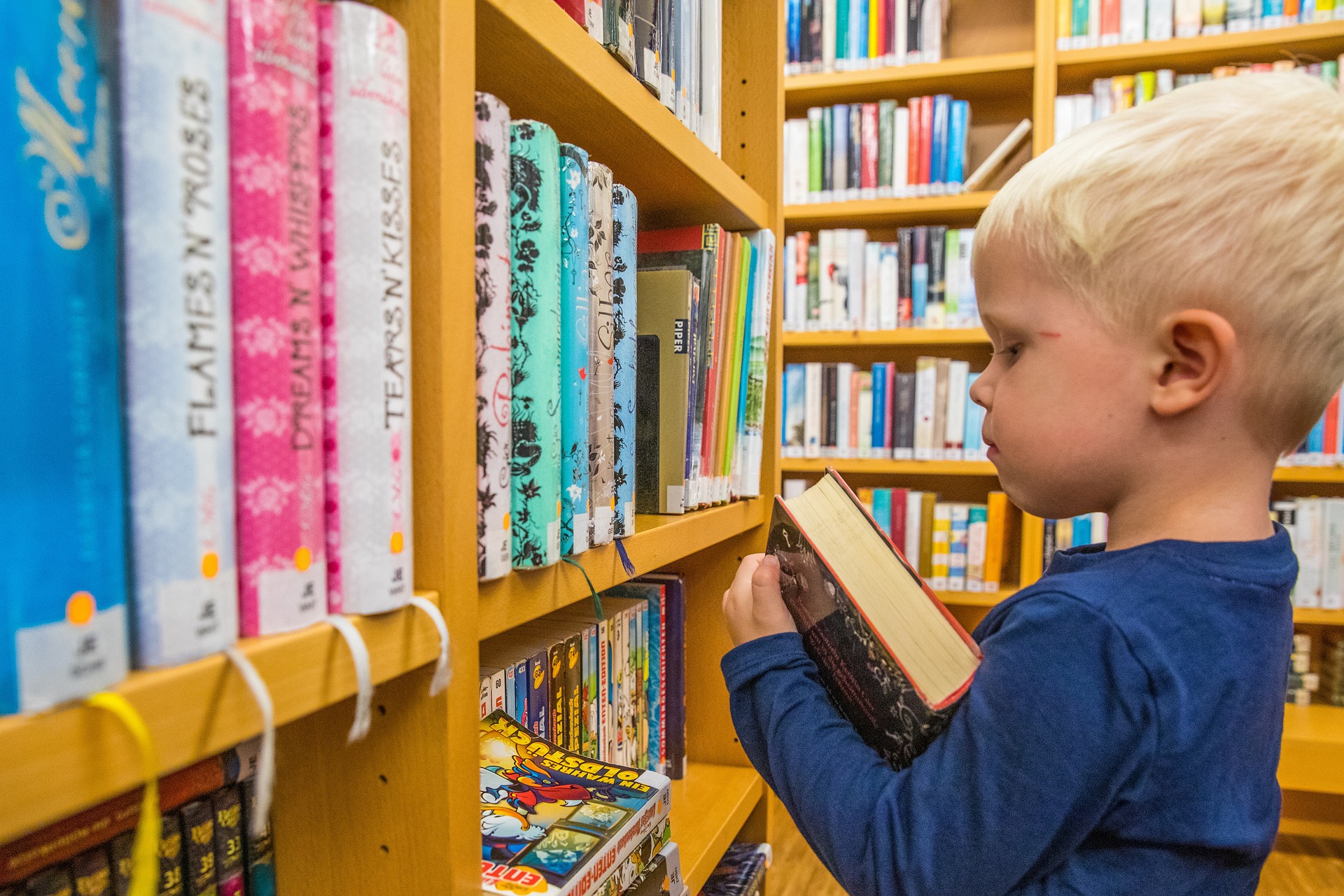 Ein Kind steht vor einem Bücherregal in einer Bücherei. Es hält ein Buch im Arm.