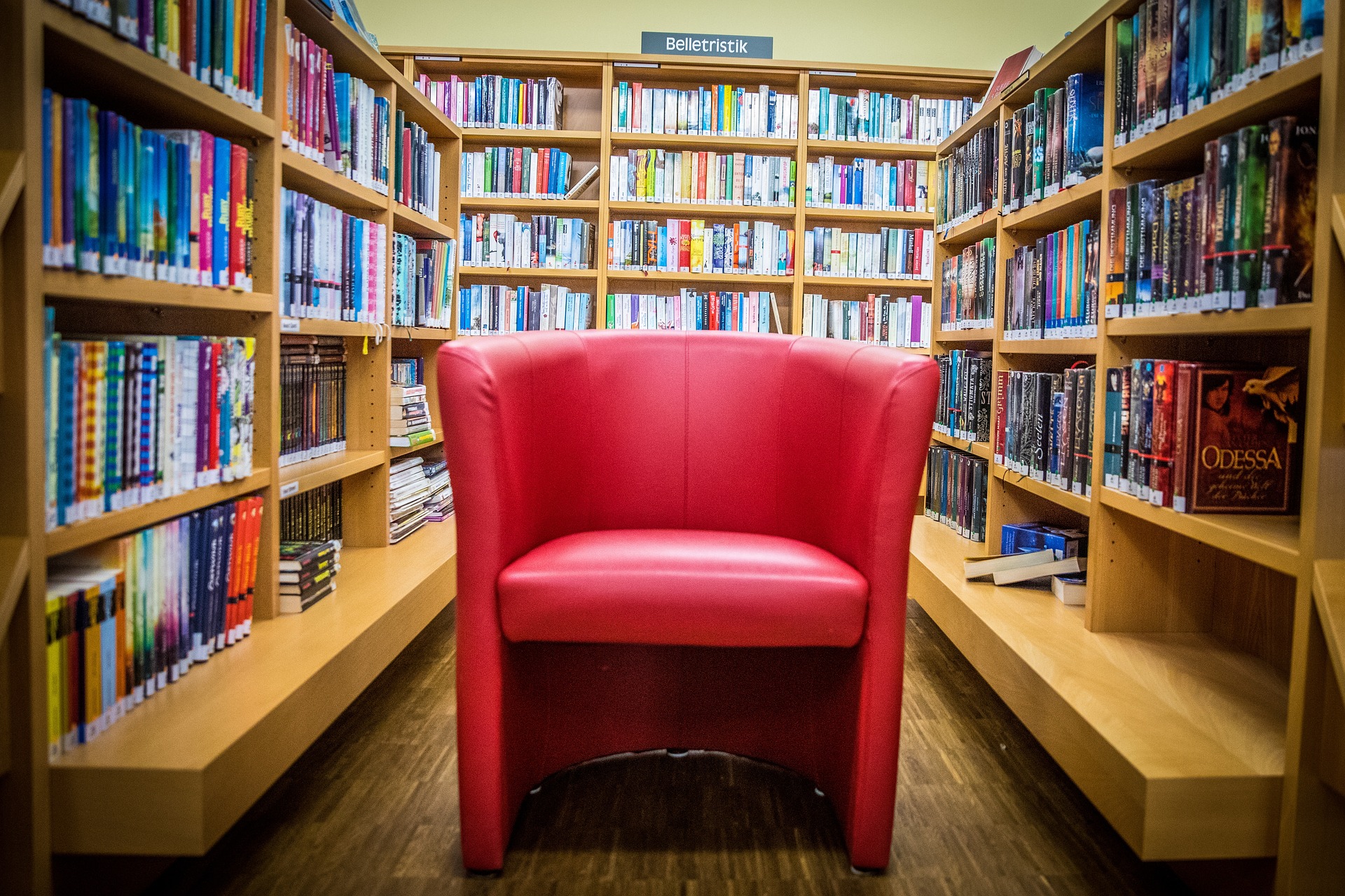 Eine Bücherei von innen, Regale mit Büchern auf drei Seiten, in der Mitte ein roter Sessel