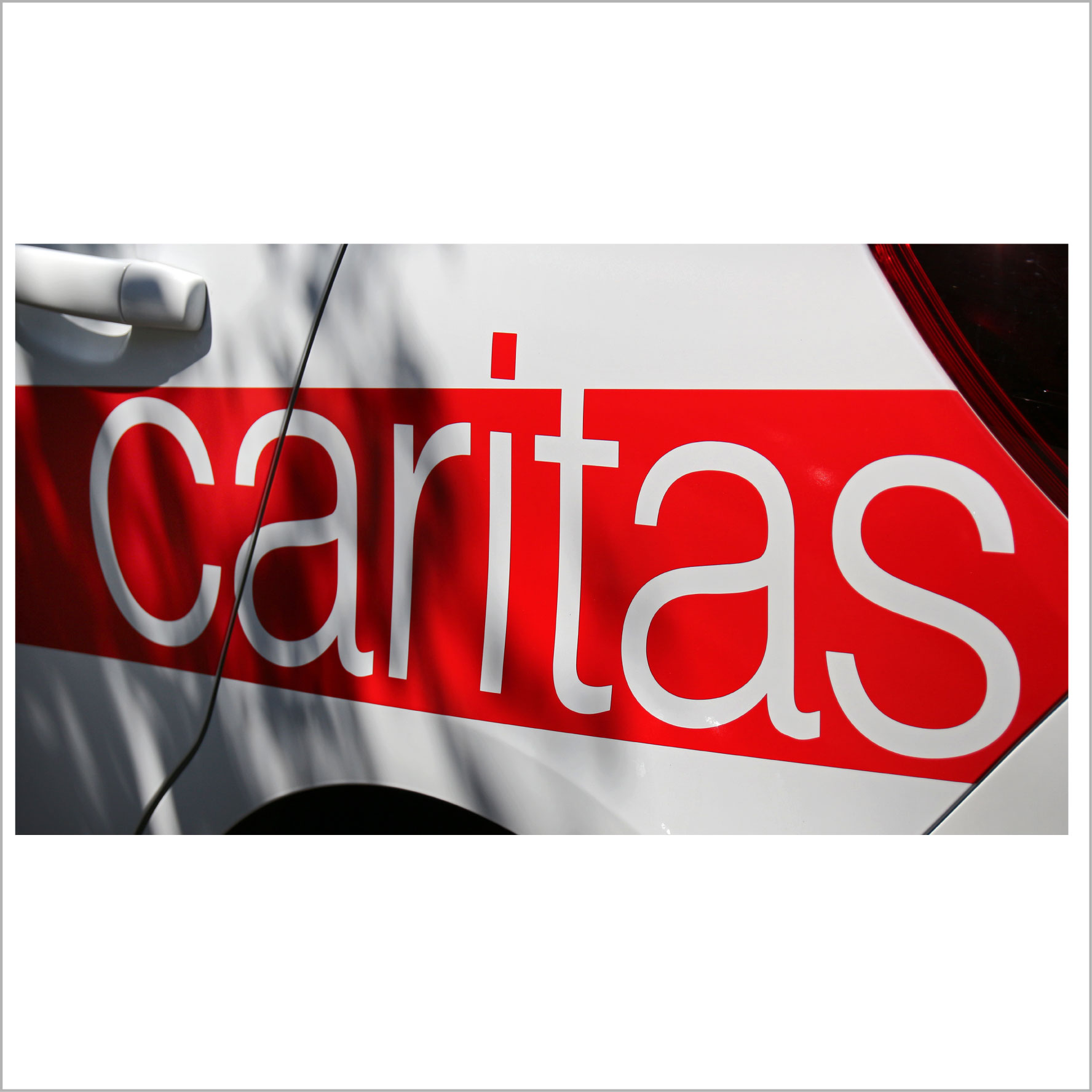 Weißer Caritas-Schriftzug auf rotem Hintergrund auf der Seite eines weißen Autos