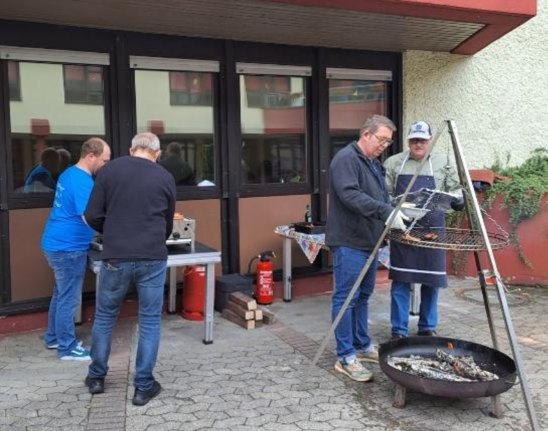 Fronleichnam 2026 - Fest der Begegnung - 4 Personen beim Grillen vor dem Jugendheim Merchweiler (c) Simone Brennauer Fronleichnam 2026 - Fest der Begegnung - 4 Personen beim Grillen vor dem Jugendheim Merchweiler