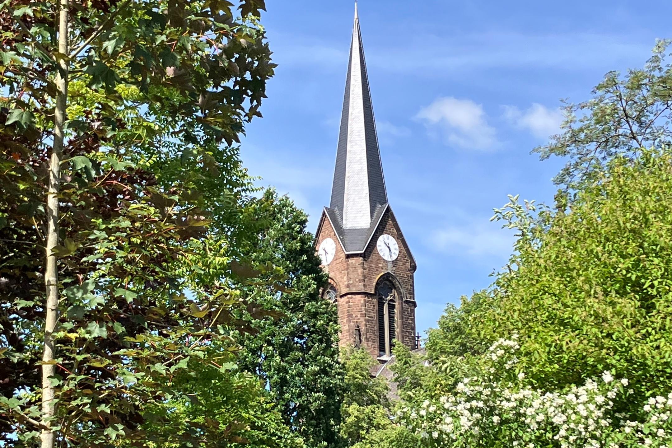 Kirchturm von der Kirche St. Michael in Wemmetsweiler im Frühling hinter Bäumen