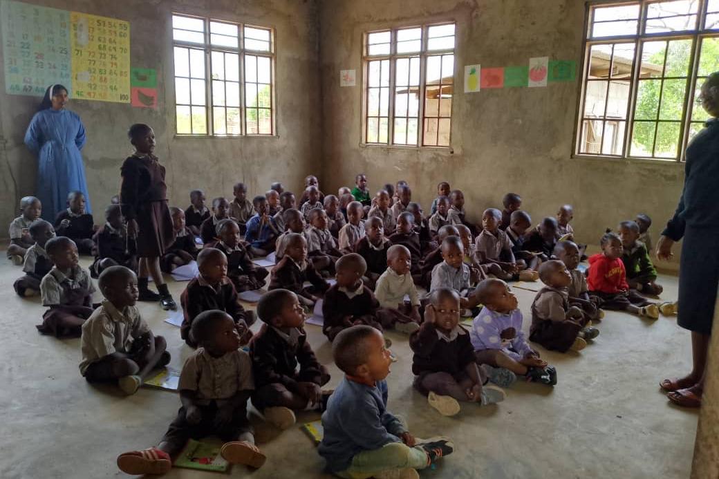 Kinder in Lupiro, Afrika, sitzen in einem Klassenraum auf dem Boden und lauschen ihrer Lehrerin (c) Pfarrei Maria Königin Merchweiler-Wemmetsweiler Kinder in Lupiro, Afrika, sitzen in einem Klassenraum auf dem Boden und lauschen ihrer Lehrerin