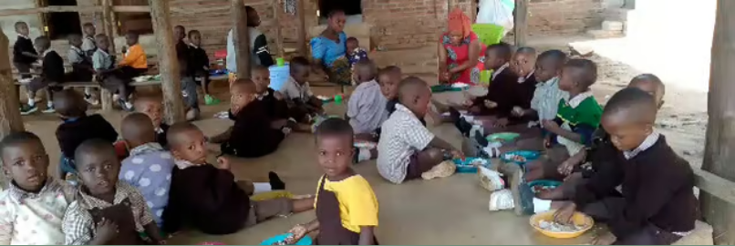 Kinder in Lupiro Tansania sitzen in der Schule aquf dem Boden und essen ihre warme Mahlzeit.