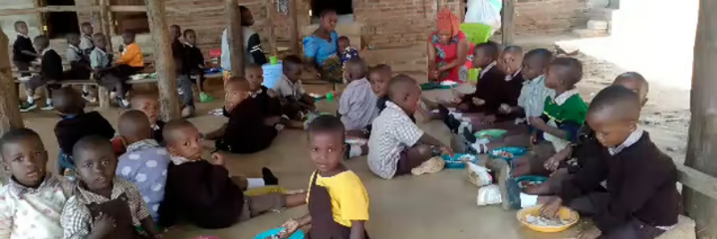 Kinder in Lupiro Tansania sitzen in der Schule aquf dem Boden und essen ihre warme Mahlzeit.
