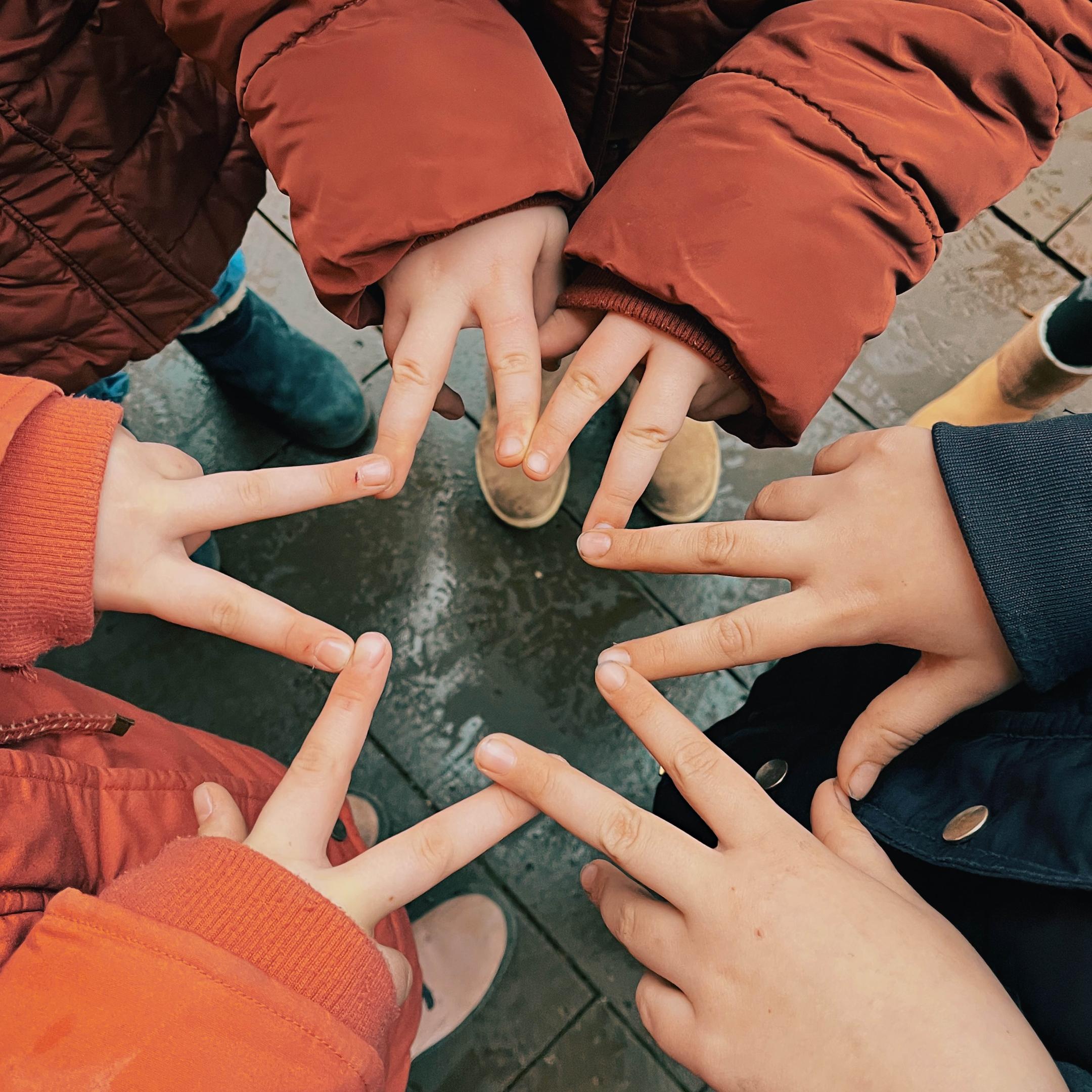 Die gespreizten Finger von drei Jugendlichen bilden einen Stern